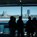 Silhouetted people enjoy a waterfront view of a modern city skyline on a clear day.